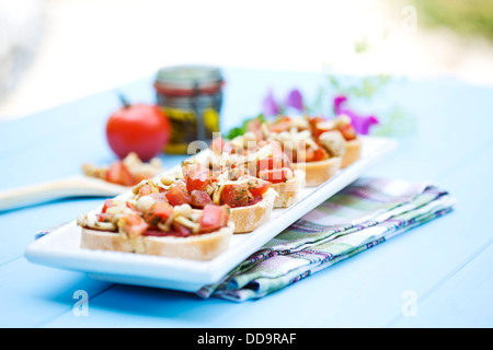 Teller mit Bruschetta mit Tomaten, weiße Shimeji Pilze, Kräuter und Olivenöl auf Holztisch, Nahaufnahme Stockfoto