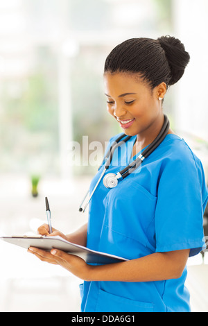 lächelnde junge afrikanische medizinische Intern Arzt schriftlich auf Zwischenablage im Büro Stockfoto