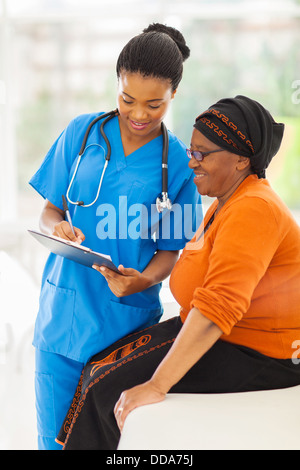 schöne junge afrikanische Krankenschwester erklärt medizinische Testergebnis für ältere Patienten Stockfoto