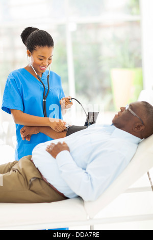 freundliche junge afrikanische Ärztin senior Patient Blutdruck überprüfen Stockfoto