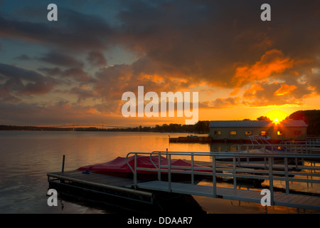 Die Sonne geht über einen Yachthafen am Sankt-Lorenz-Strom mit der Thousand Islands Bridge im Hintergrund in Alexandria Bay, New York Stockfoto