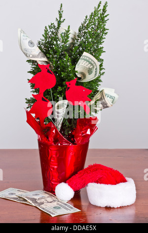 kleiner Weihnachtsbaum mit 20-Dollar-Scheine wachsen aus ihm heraus und eine Weihnachtsmütze Stockfoto