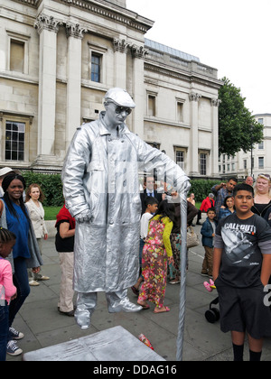 Straßenkünstler Straßenmusiker in Silber gekleidet und scheinbar in der Luft, ausgesetzt unterhält eine Menschenmenge am Trafalgar Square in London Stockfoto