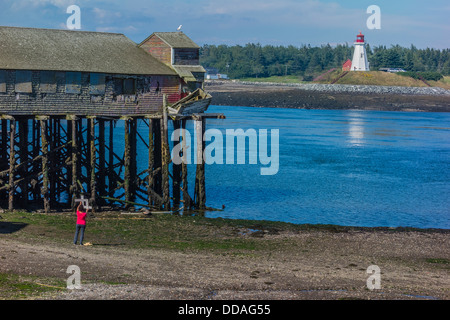 Eine weibliche Künstlerin verwendet eine Zuschneidetool um den besten Blick auf eine Fischverarbeitung Gebäude auf Stelzen & Leuchtturm für ein Gemälde zu finden. Stockfoto