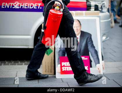 Ein Mitarbeiter der deutschen Sozialdemokratischen Partei (SPD) hält einen Feuerlöscher, wie er vorbei ein Wahlplakat der SPD-Kanzlerkandidat Steinbrück in Langenfeld, Deutschland, 23. August 2013 geht. Foto: Jan-Philipp Strobel Stockfoto