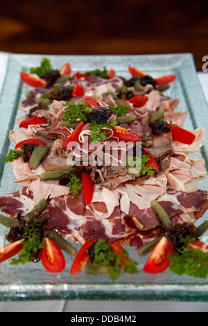 Dünne slicese aus einer Vielzahl von Fleisch auf große rechteckige Glas platemon weiße Tischdecke auf dem Tisch Huhn Rind Schwein Speck Pfeffer Tomaten serviert. Stockfoto
