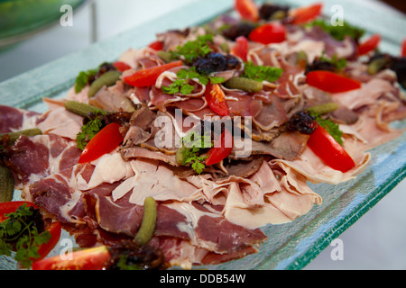 Dünne slicese aus einer Vielzahl von Fleisch auf große rechteckige Glas platemon weiße Tischdecke auf dem Tisch Huhn Rind Schwein Speck Pfeffer Tomaten serviert. Stockfoto