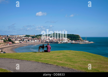 Mann und Hund schauen im Sommer über South Bay Scarborough Seaside Küstenresort Blick auf North Yorkshire England Großbritannien Großbritannien Großbritannien Großbritannien Großbritannien Großbritannien Großbritannien Großbritannien Großbritannien Großbritannien Großbritannien Großbritannien Stockfoto