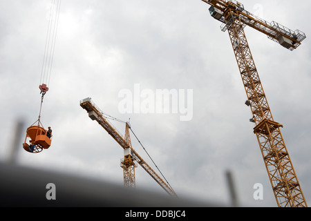 Turmdrehkran heben einen Arbeiter einen Eimer mit nassem Beton auf einer Baustelle in Düsseldorf tätig Stockfoto