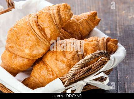 Croissants in Korb auf Holztisch Stockfoto