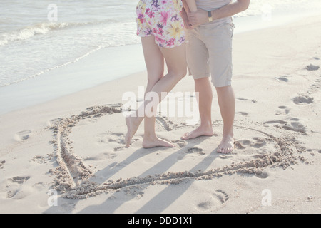 Die Form eines Herzens in den Sand gezeichnet. Paar steht im inneren Herzen Bild auf dem Sand. Sommerspaß Stockfoto