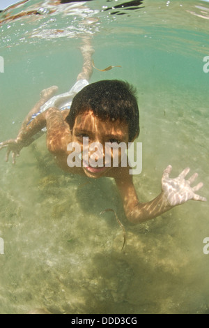 Ein kleiner Junge lächelt in die Kamera, als er in der Karibik schwimmt. Stockfoto