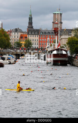 Kopenhagen, Dänemark. August 2013. 2.400 Schwimmen rund um das Parlamentsgebäude, den Schloss Christiansborg im Zentrum Kopenhagens im 2.000 m größten jährlichen Open-Water-Wettbewerb in Dänemark, der vom dänischen Schwimmverband und der Zeitung Politik veranstaltet wird. Dies befindet sich im Frederiksholm Canal auf der letzten Strecke kurz vor dem 80-m-Tunnel, den die Schwimmer wegen Bauarbeiten in Kopenhagen durchschwimmen müssen. Die Kirchtürme der St. Petri Kirche und der Kopenhagener Kathedrale, Vor Frue Kirke, von links im Hintergrund. Altes Feuerschiff als Hausboot. Kredit: Niels Quist/Alamy Live News Stockfoto