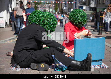 Runde, runde, grüne Kopfbedeckung, baumbestandene künstliche Perücken, Kopfanlage, getragen von Straßenkünstlern in Kendal, Cumbria, Großbritannien. August 2013. Mintfest, Kendal's International Festival of Street Arts, The Potheads by Let's Circus, Fat Face Shop, ein Lakes Alive Weekend Event im Lake District, bei dem einige der besten aus der ganzen Welt auftraten, zeitgenössischer Tanz, Zirkus, Comedy, Musik, Eigenartige Gruppe draußen auf den Straßen. Stockfoto