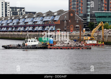 Arbeiten zur Reparatur des eingestürzten Gehwegs am Anderston Quay am Fluss Clyde mit einem Bagger, der von einem Lastkahn in Glasgow, Schottland, Großbritannien, arbeitet Stockfoto