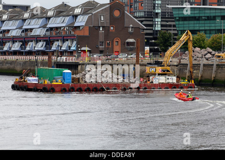 Arbeiten zur Reparatur des eingestürzten Gehwegs am Anderston Quay am Fluss Clyde mit einem Bagger, der von einem Lastkahn in Glasgow, Schottland, Großbritannien, arbeitet Stockfoto