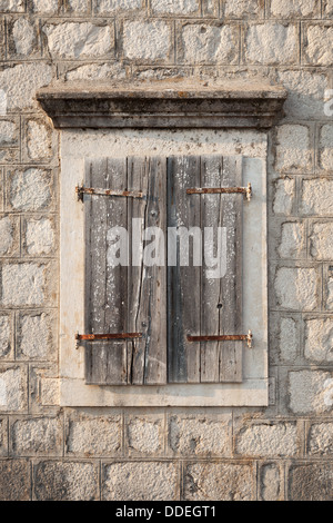 Alte Fenster mit geschlossenen hölzernen Jalousien in grauen Steinwand. Perast Stadt, Montenegro Stockfoto