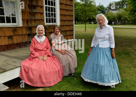 Alten Bethpage, New York, USA 31. August 2013.  JANE HEILIG der Bethpage, Taupe und Schwestern PATRICIA JOSEPH College Point in rot und JULIETTE FOX von Hicksville in blau, Bürgerkrieg Ära Stil des 19. Jahrhunderts Kleidung tragen und sind Mitglieder der alten Bethpage Dorf Tänzer die ganze Olde Zeit Musik Wochenende am alten Bethpage Village Restaurierung getanzt. Sie sind auf der Veranda von 12 Lawrence House. Stockfoto