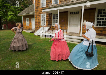 Alten Bethpage, New York, USA 31. August 2013.  JANE HEILIG der Bethpage, Taupe und Schwestern PATRICIA JOSEPH College Point in rot und JULIETTE FOX von Hicksville in blau, Bürgerkrieg Ära Stil des 19. Jahrhunderts Kleidung tragen und sind Mitglieder der alten Bethpage Dorf Tänzer die ganze Olde Zeit Musik Wochenende am alten Bethpage Village Restaurierung getanzt. Sie sind auf der Veranda von 12 Lawrence House. Stockfoto