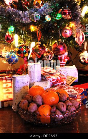 Glasschale gefüllt mit Walnüssen, Haselnüssen und Mandarinen mit Weihnachten präsentiert unter Baum nach hinten. Stockfoto