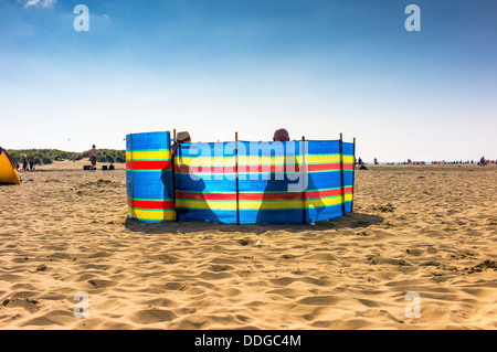 Ein älteres paar Sit Silhouette hinter einem Windschutz am Strand, der Hut und seine Glatze sichtbar über der Oberseite, Stockfoto