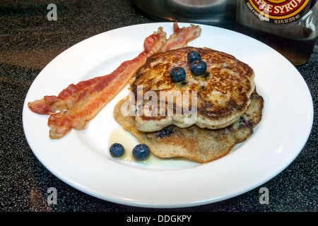 Weißen Teller mit zwei großen Heidelbeer-Pfannkuchen mit Heidelbeeren, Ahornsirup sowie zwei Streifen Speck gekrönt. Stockfoto