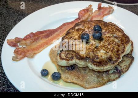 Weißen Teller mit zwei großen Heidelbeer-Pfannkuchen mit Heidelbeeren, Ahornsirup sowie zwei Streifen Speck gekrönt. Stockfoto