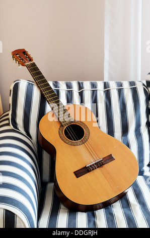 akustische Gitarre auf einem gestreiften Sofa, vertikale Stockfoto