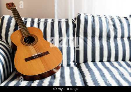 akustische Gitarre auf einem gestreiften Sofa, horizontale Stockfoto