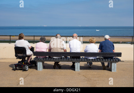 Rückansicht von sechs älteren Menschen, die an einem sonnigen Tag in Redcar an der Nordostküste Englands auf das Meer blicken. VEREINIGTES KÖNIGREICH Stockfoto