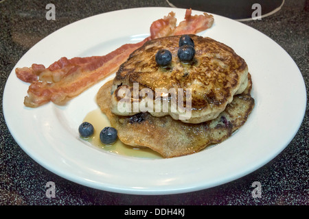 Weißen Teller mit zwei großen Heidelbeer-Pfannkuchen mit Heidelbeeren, Ahornsirup sowie zwei Streifen Speck gekrönt. Stockfoto