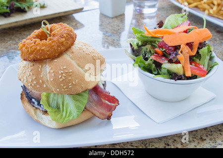 Hamburger mit Zwiebel Ring Schinken Rindfleisch Patty Salat und Schale von Bio-Gemüse-Salat Stockfoto