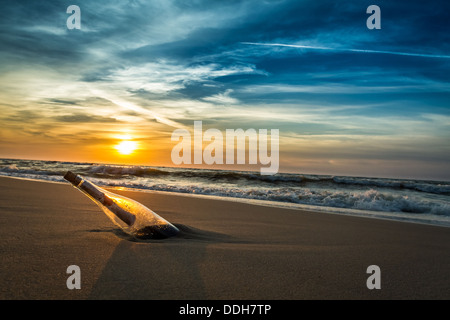 Nachricht mit Brief in der Flasche an einem Strand im Sonnenuntergang Stockfoto