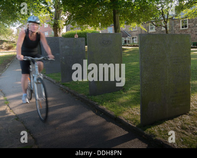 Frau mit dem Fahrrad vorbei an Grabsteine auf einem kirchlichen Friedhof. Stockfoto