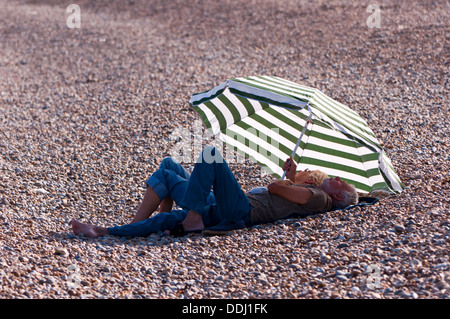 Rentner sitzen unter Sonnenschirm am Strand Stockfoto