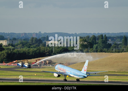 Ein Thomson Boeing 757 Flugzeug hebt ab, während ein Flughafen Feuerwehrauto Sprays Wasser im Hintergrund.