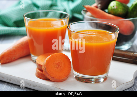 Gläser Karottensaft und frische Karotten auf Holzbrett Stockfoto