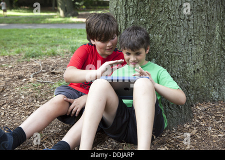 Zwei junge Freunde, ein Spiel auf einem Ipad zusammen in den Park, Brooklyn, NY. Stockfoto