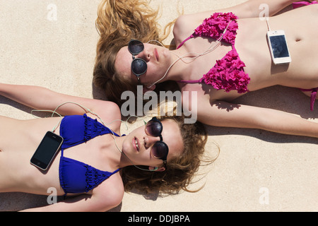 Zwei Mädchen im Teenageralter liegen in der Sonne, die Musik auf ihrem Handy anhören. Stockfoto