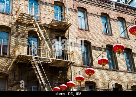 Backsteinbau mit Feuerleiter in Chinatown, San Francisco mit roten Lampions geschmückt. Stockfoto