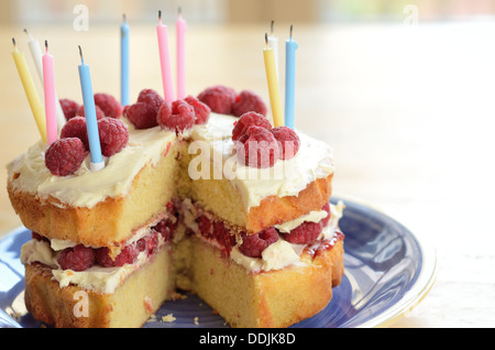 Geburtstagskuchen hausgemacht mit Schwamm, Himbeeren, Sahne und Kerzen auf einen blauen Teller und Tisch aus Holz Stockfoto