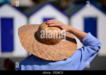 Damen statt Strohhut auf gegen die Brise mit Hintergrund Meer Strand Hütten Stockfoto