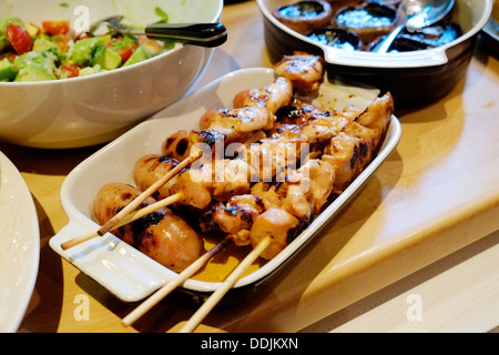 Eine köstliche Platte mit gegrillten Hähnchen am Spieß mit gegrillten Champignons und Avocado Tomatensalat im Hintergrund. Stockfoto