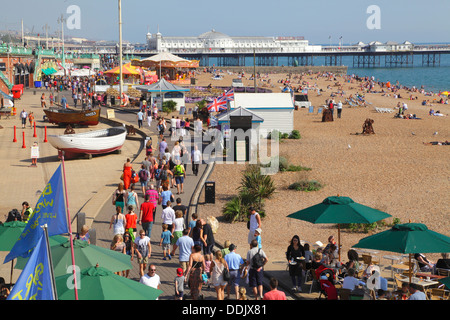 Menschen zu Fuß auf Brighton Promenade und Sonnenbaden am Strand East Sussex England UK Stockfoto