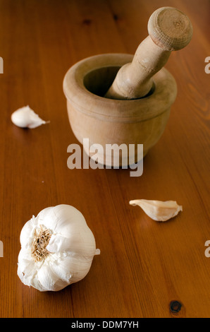 Knoblauch im Vordergrund und hinter hölzernen Mörtel auf einem Holztisch Stockfoto