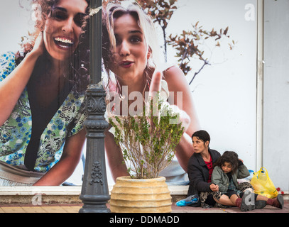 Roma-Frau und Kind betteln neben einer Werbung Horten in der provinziellen Stadt Zacharo, Peloponnes, Griechenland Stockfoto