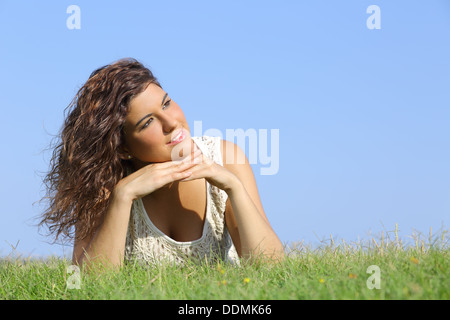 Porträt einer schönen Frau liegend auf dem Rasen mit einem blauen Himmel im Hintergrund Stockfoto