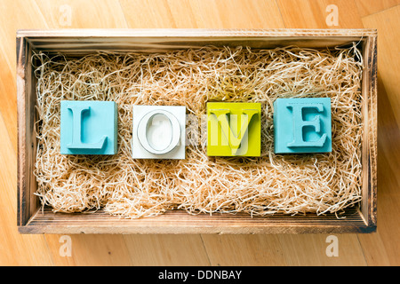 Das Wort Liebe buchstabiert in großen Druckbuchstaben in einer hölzernen Geschenkbox gefüllt mit Bast Stockfoto