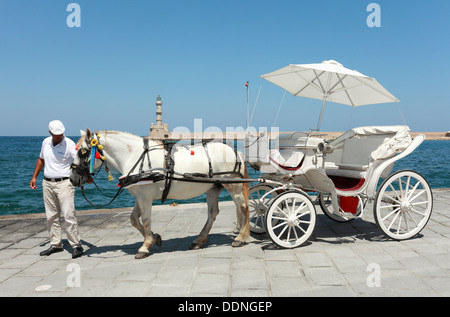 Ein Pony und Buggy am Strand von Chania, Kreta, Griechenland, mit dem Leuchtturm im Hintergrund. Stockfoto