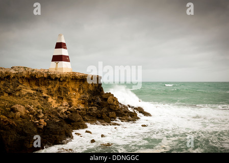 Leuchtturm auf einer Klippe mit Wellen, die unter einem Gewitterhimmel Stockfoto